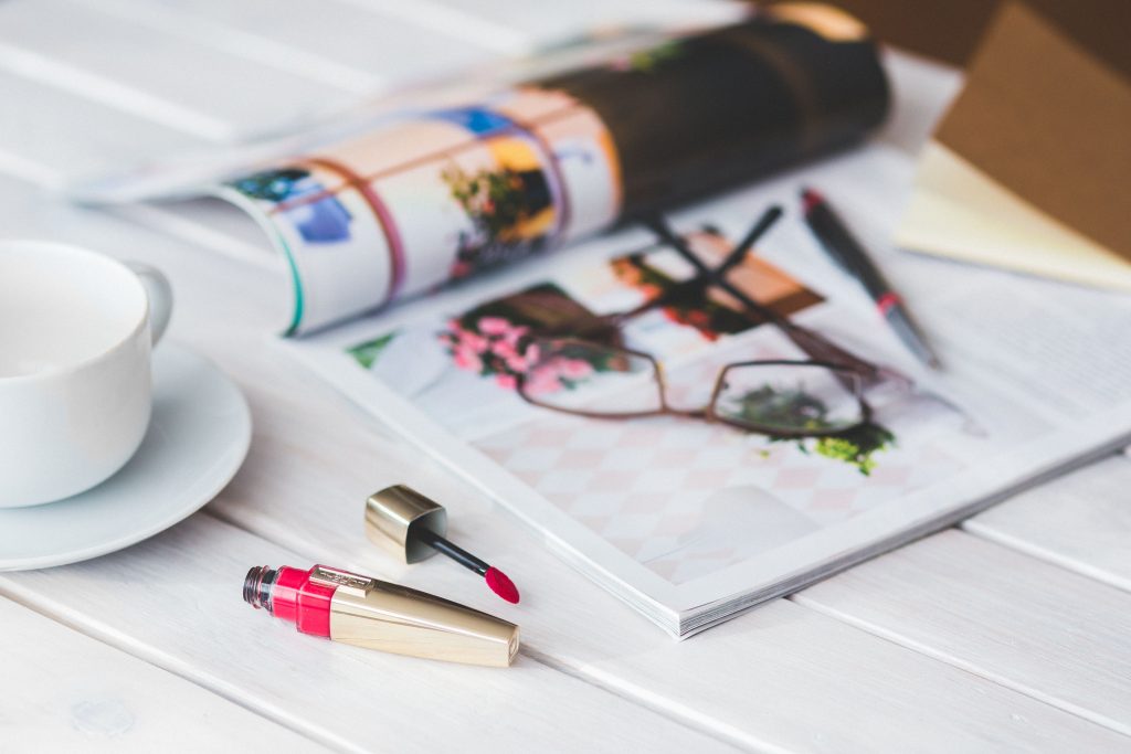 Stylish flat lay of makeup, magazine, and coffee cup on a light wooden table.